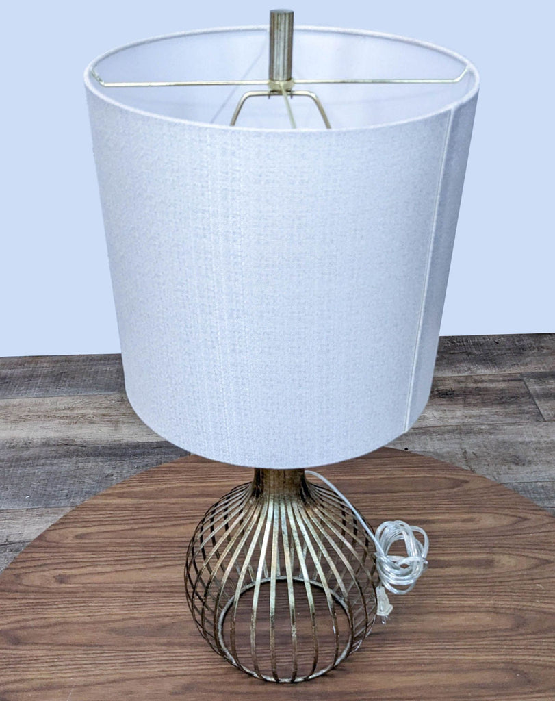 Stylish lamp with a metal cage base and cylindrical shade on a wooden table.