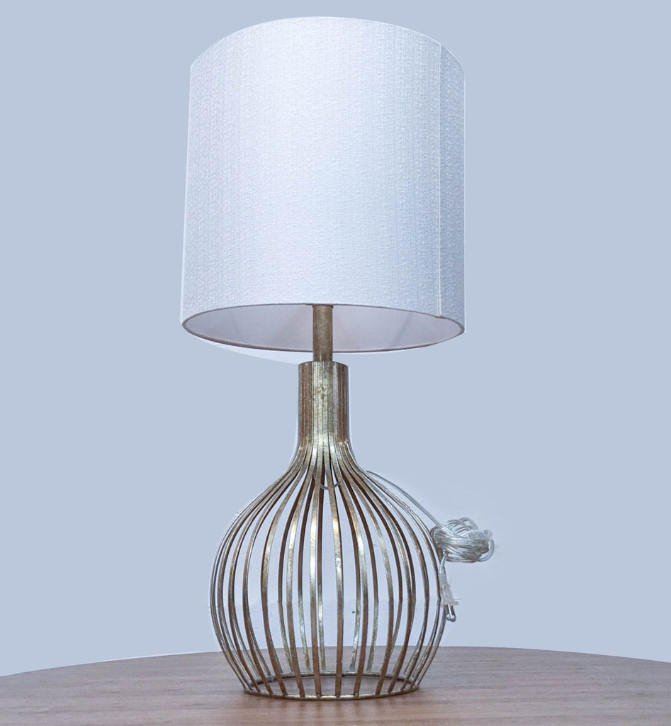Modern table lamp with a white shade and metal cage base on a wooden surface.