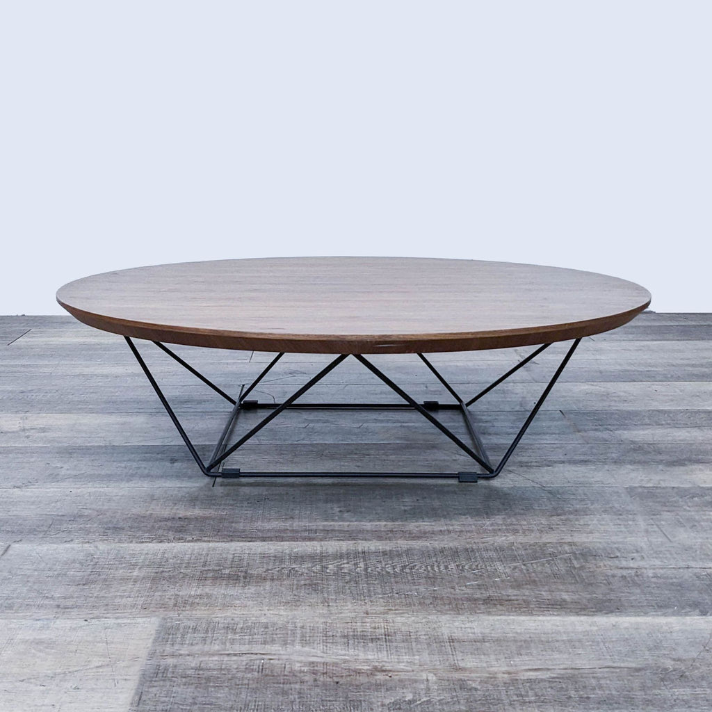 Round wooden coffee table with geometric metal legs seen from the side.