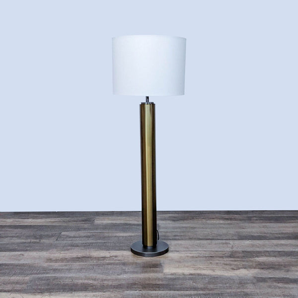 Floor lamp with a brass base and white drum shade on wooden flooring.