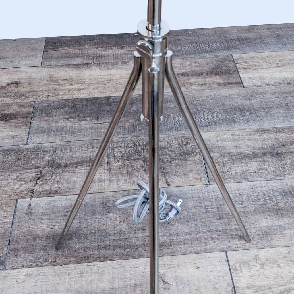 Close-up of the Reperch lamp's shiny metal tripod base on wood floor.