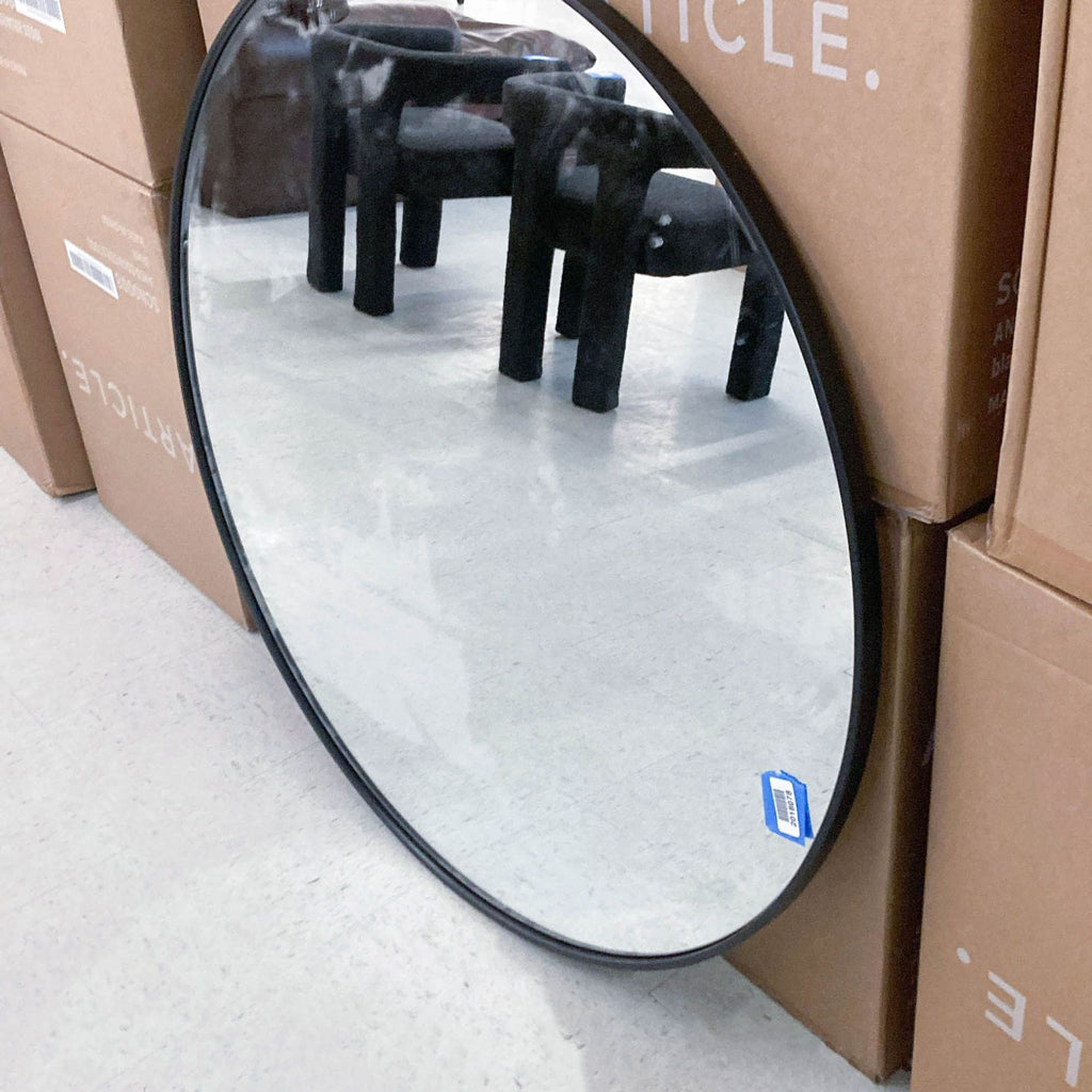 2. Reperch round mirror with a black frame, leaning on boxes and reflecting black chairs.