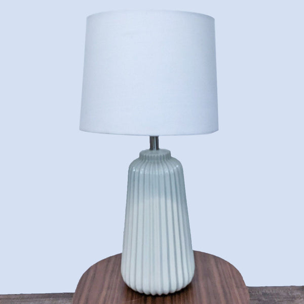Reperch lamp with ribbed ceramic base and white shade, set on a wooden surface.