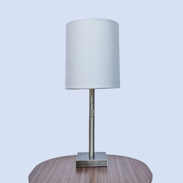 Modern table lamp with a white shade and sleek metal base on a wooden surface.