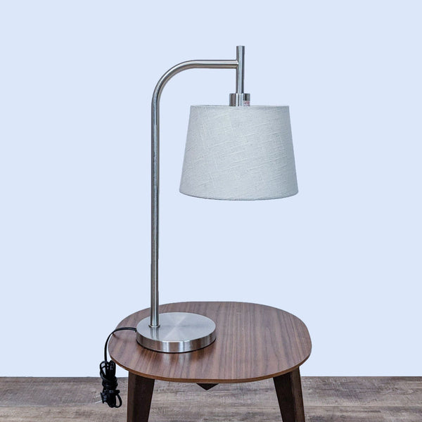 Reperch lamp with a curved metallic stand and white fabric shade on a wooden table.