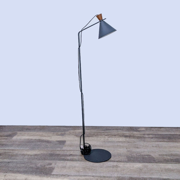 Sleek black floor lamp with a minimalist design and cone-shaped shade, on a wooden floor.