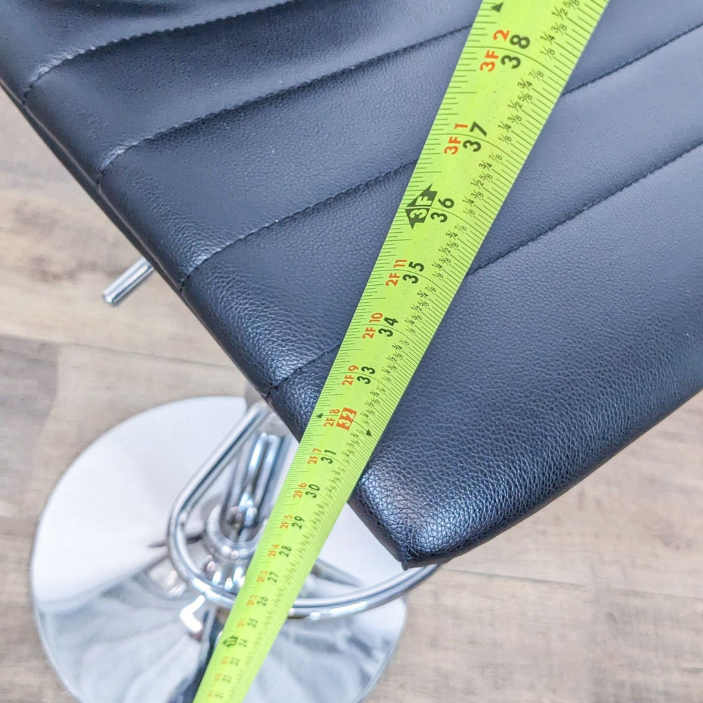 Close-up of Reperch swivel stool seat with a measuring tape across black leather-look fabric.