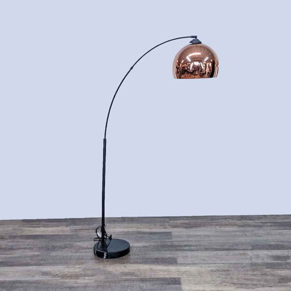 Reperch lamp with arched black stand and copper dome shade on a wooden floor.