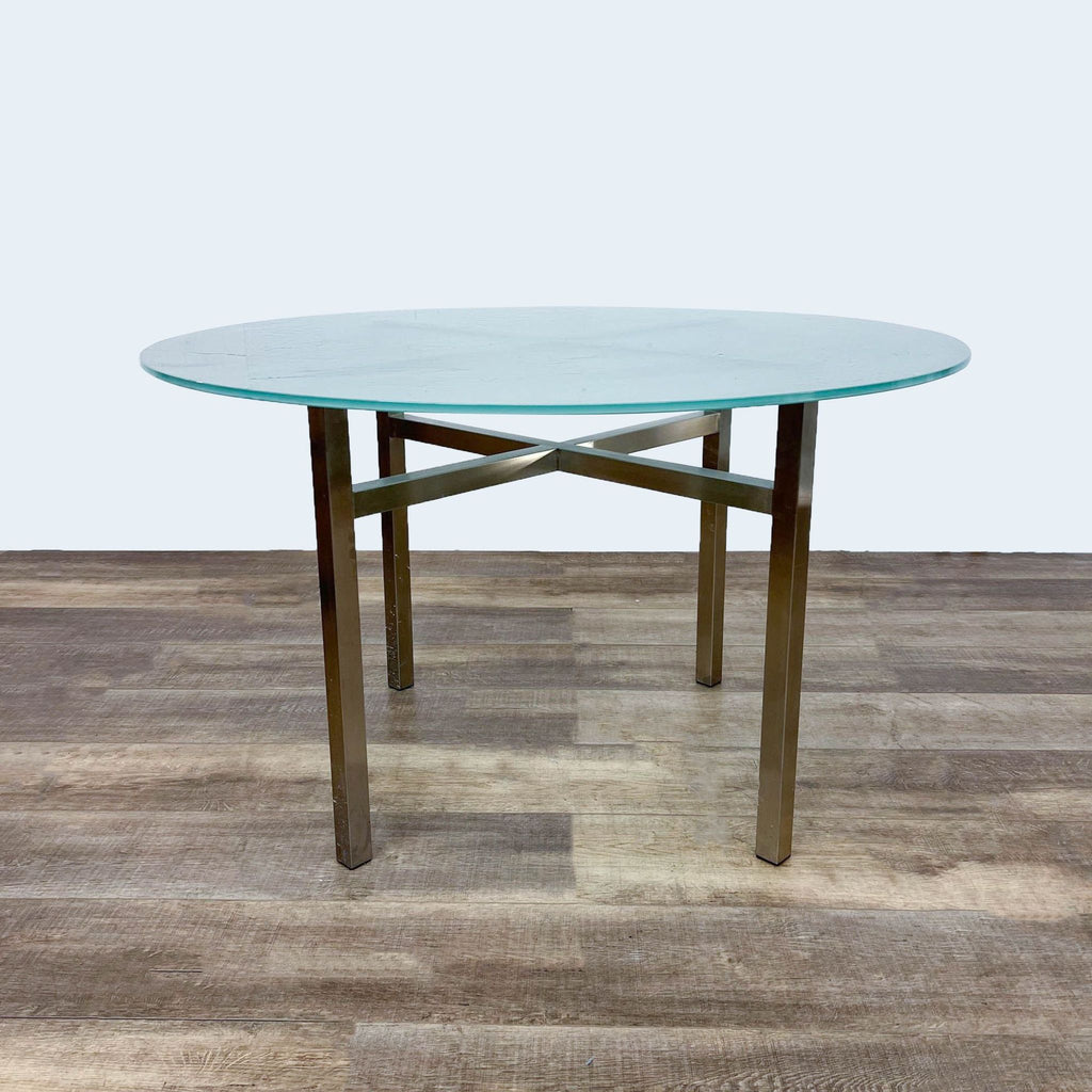 Round frosted glass dining table with gold metal cross brace base.