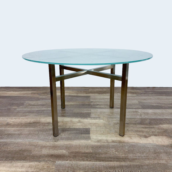 Round frosted glass dining table with gold metal cross brace base.