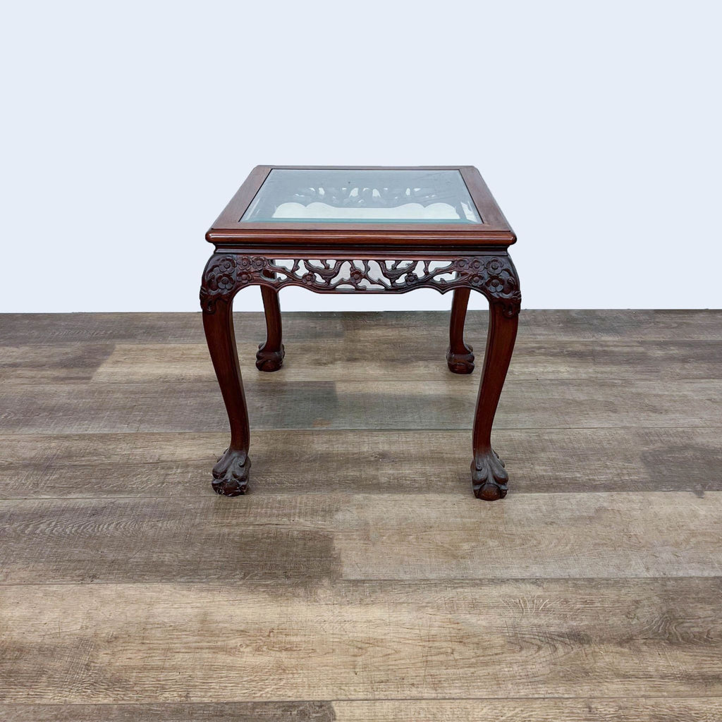 Elegant end table by Reperch features claw feet and intricate woodwork beneath a glass top.