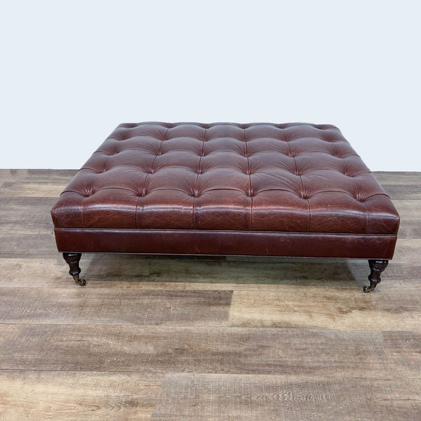 Tufted leather ottoman with spindle feet and metal casters on wood floor.  