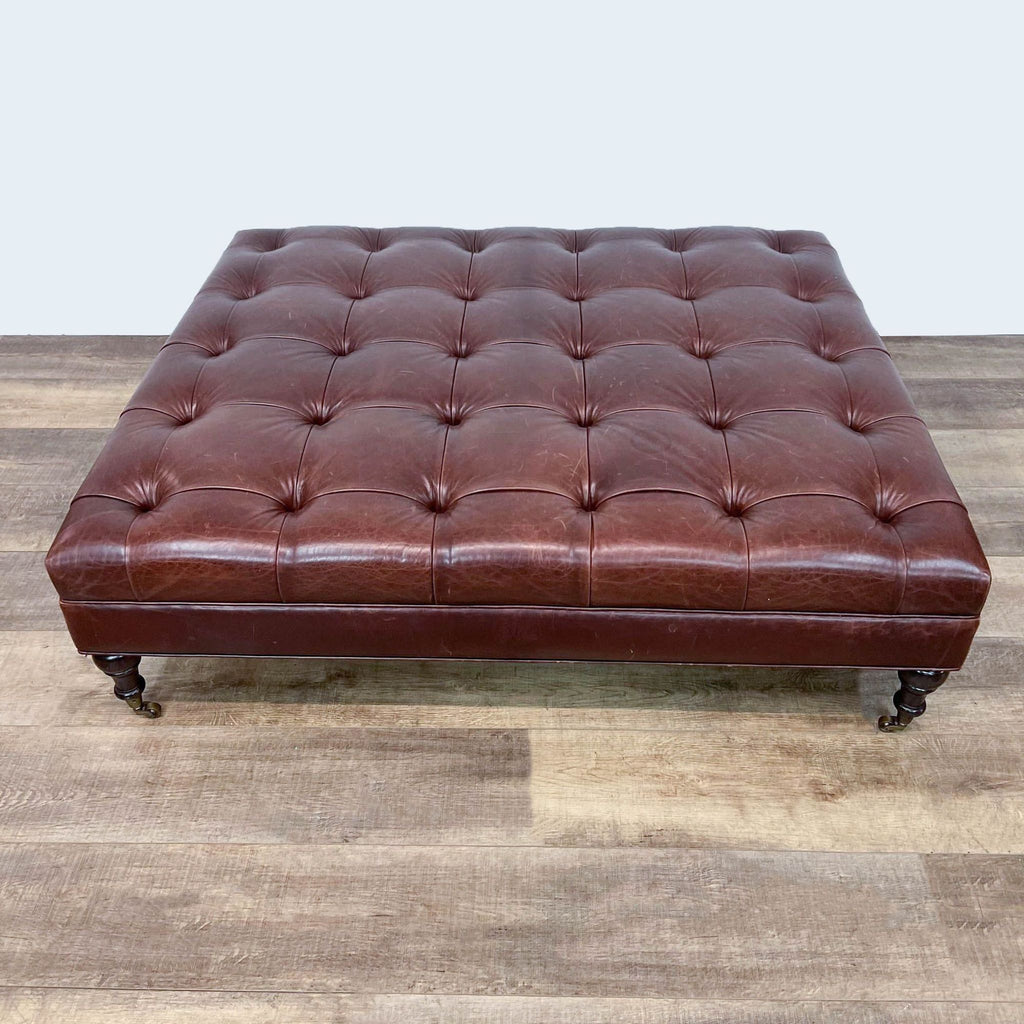 Square tufted leather ottoman with dark spindle feet on casters.