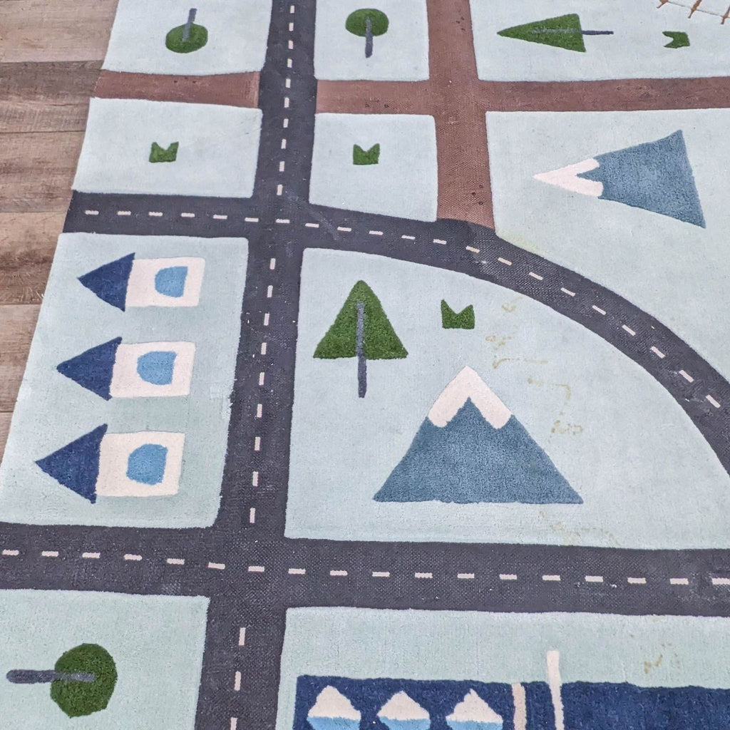 Close-up of wool rug design featuring roads, trees, mountains, and houses.