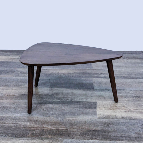 Triangular wooden coffee table from Zuo Modern with three legs on a textured floor.