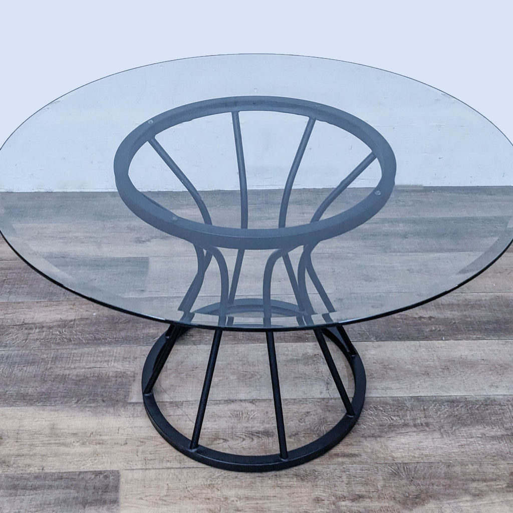 Armen Living round dining table features a black metal sculptural base and tempered glass top.