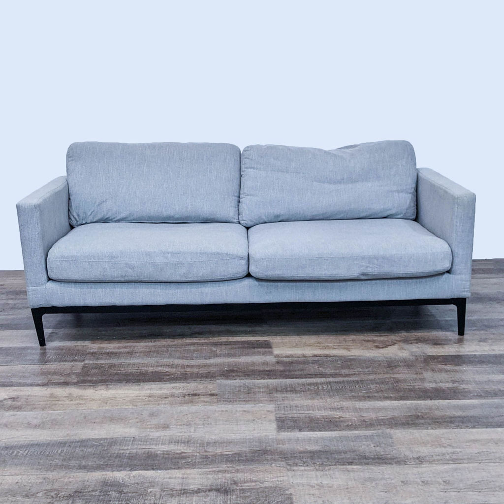 Modern gray sofa with narrow arms and metal feet on a wooden floor.