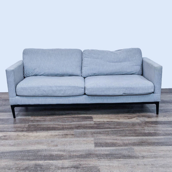 Modern gray sofa with narrow arms and metal feet on a wooden floor.