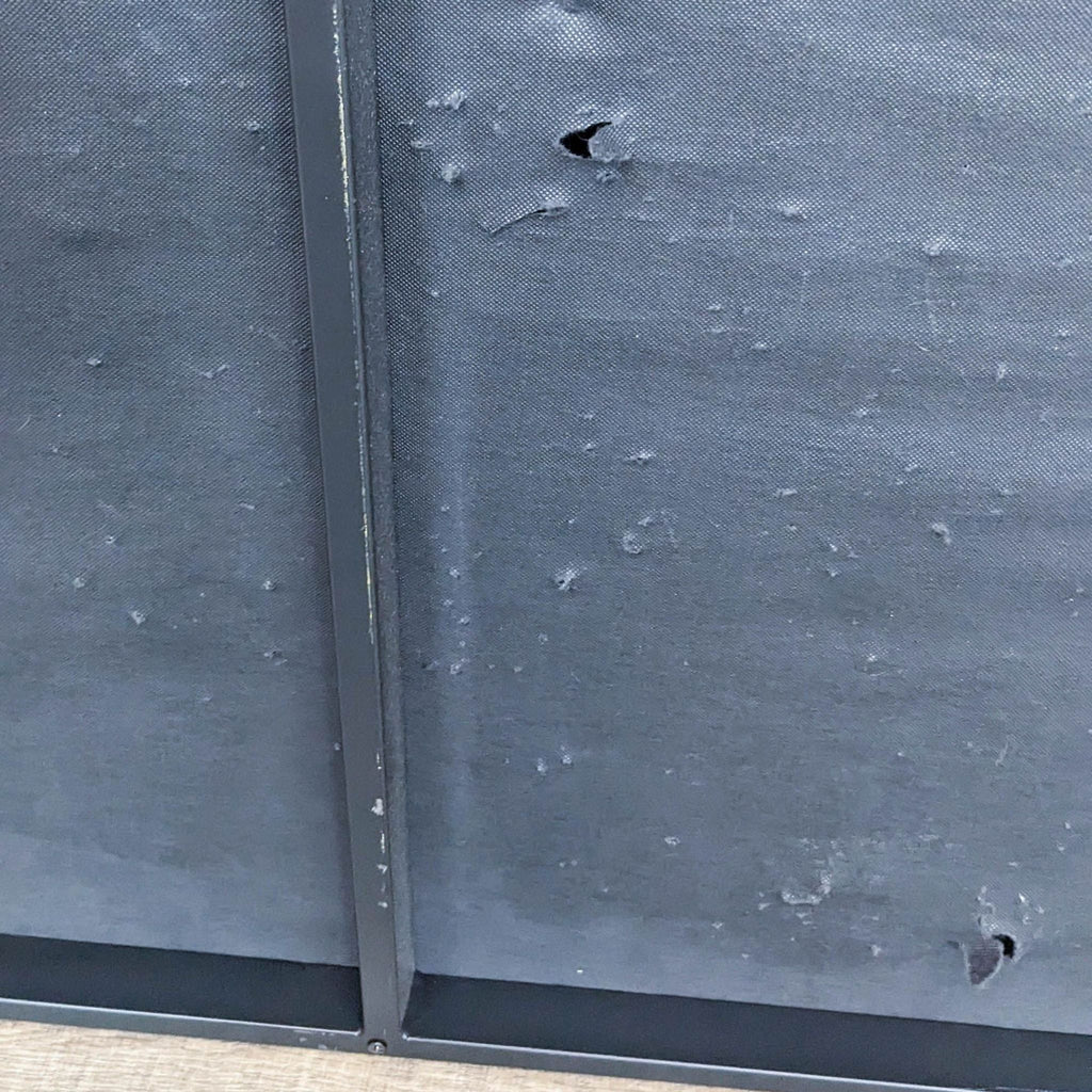 Close-up of a black metal frame with noticeable fabric wear and small holes.