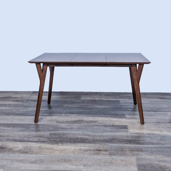 Mid-century dining table with tapered legs and beveled edges on a wood floor.  