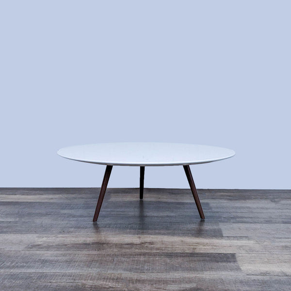 A round coffee table with a sleek MDF lacquered top and tripod base with wooden legs.