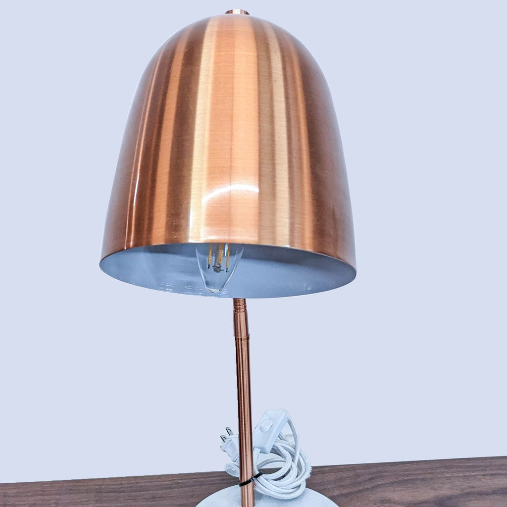 Close-up of a copper lamp's shade and bulb on a wooden table, brand Reperch.