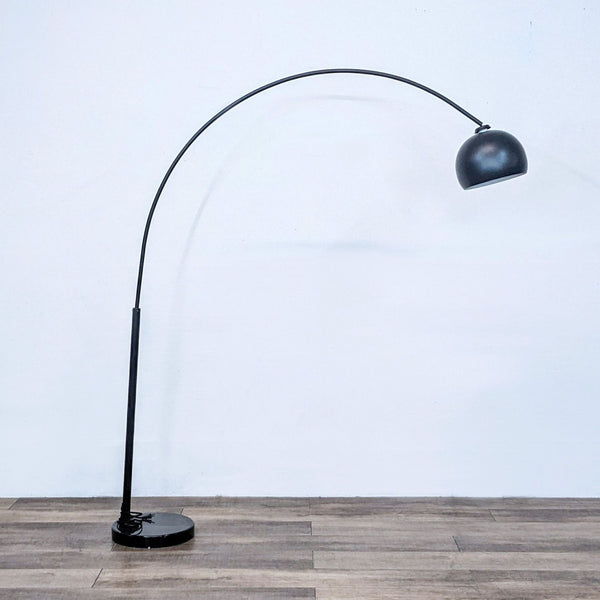 Sleek black arch floor lamp by Reperch, with a curved design on wooden flooring.