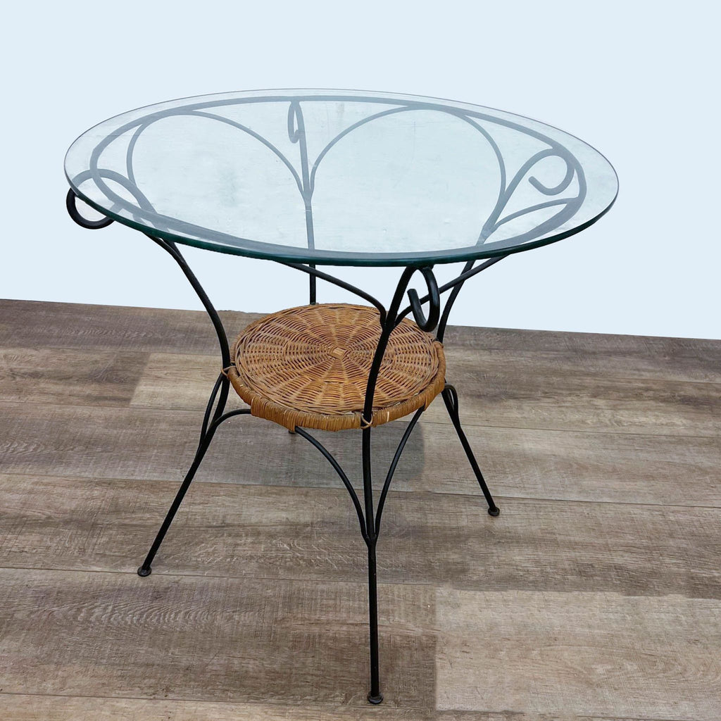 Glass bistro table with a decorative metal frame and wicker detail, at an angle.