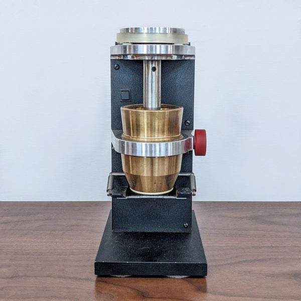 Compact black appliance on table with brass components, front view.