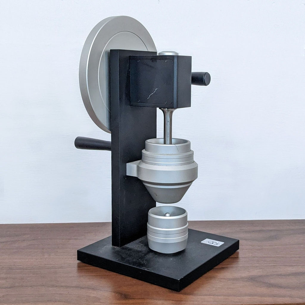 2. Side view of a black metal apparatus featuring a circular handle and stacked silver parts.