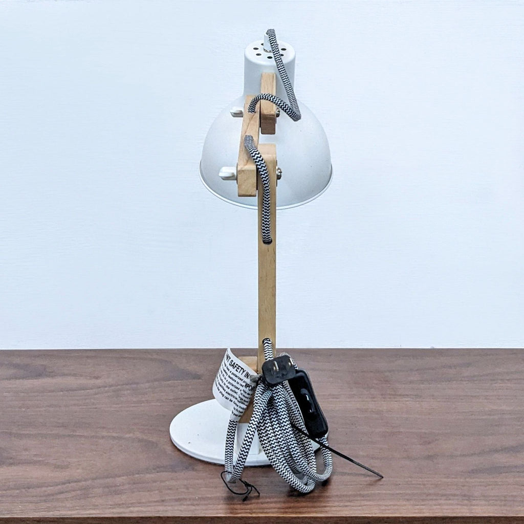 Front view of desk lamp with wooden arm and coiled cord.