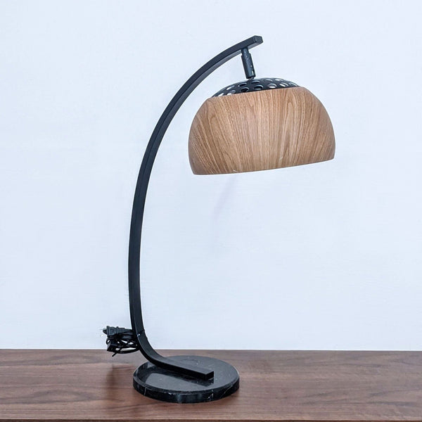 Sleek desk lamp with a curved black frame and wooden shade by Zou Modern.