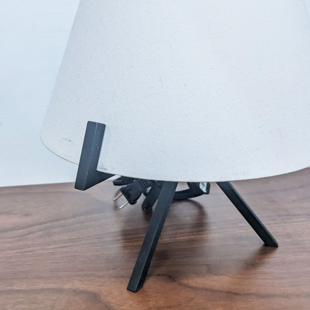Side view of Reperch lamp featuring a white shade and black tripod stand on wood.