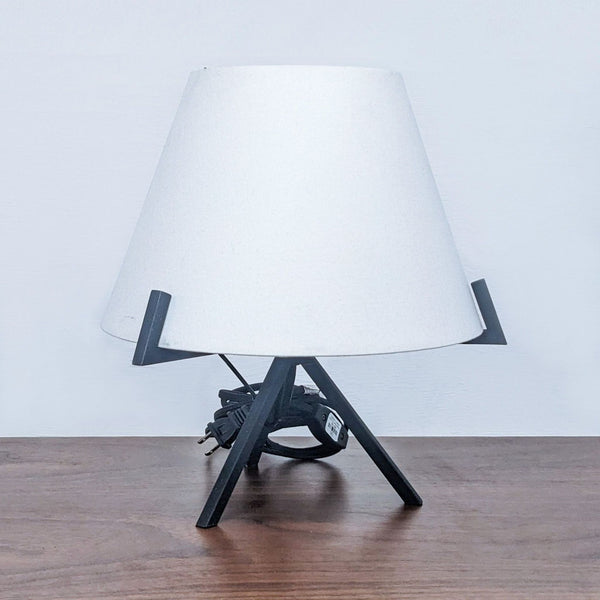Reperch lamp with a white shade and black tripod stand on a wooden surface.