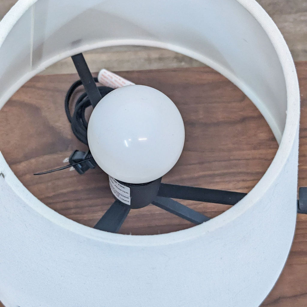 Top view of Reperch lamp highlighting the bulb within the white shade on a wooden table.