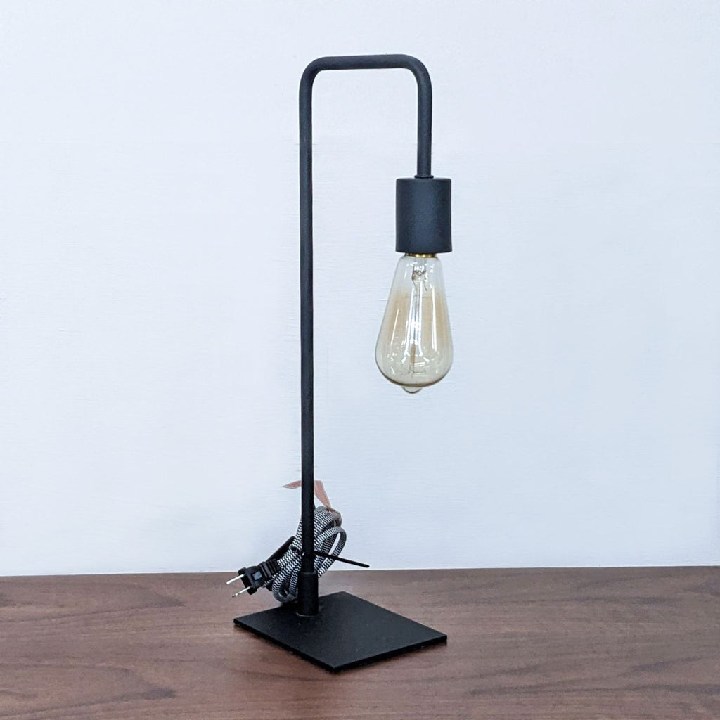 Modern black lamp with a vintage bulb, coiled cord beside it on a table.