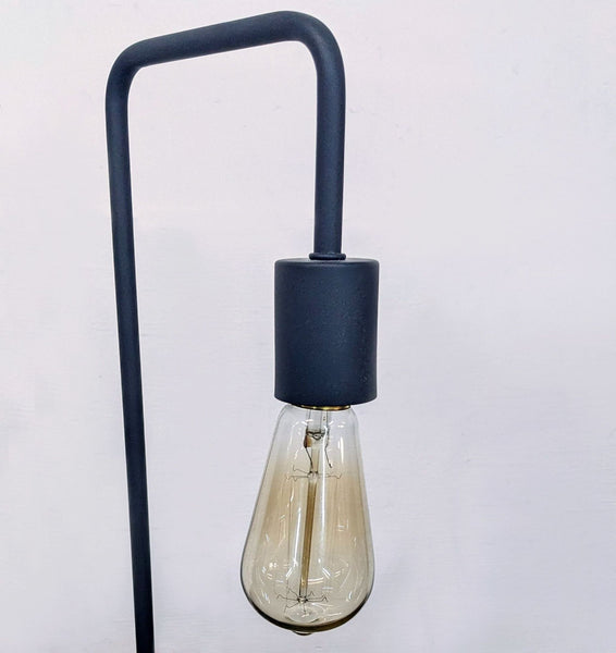 Black metal lamp with an exposed bulb on a white background.