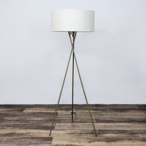 Modern floor lamp with brass tripod base and white drum shade.