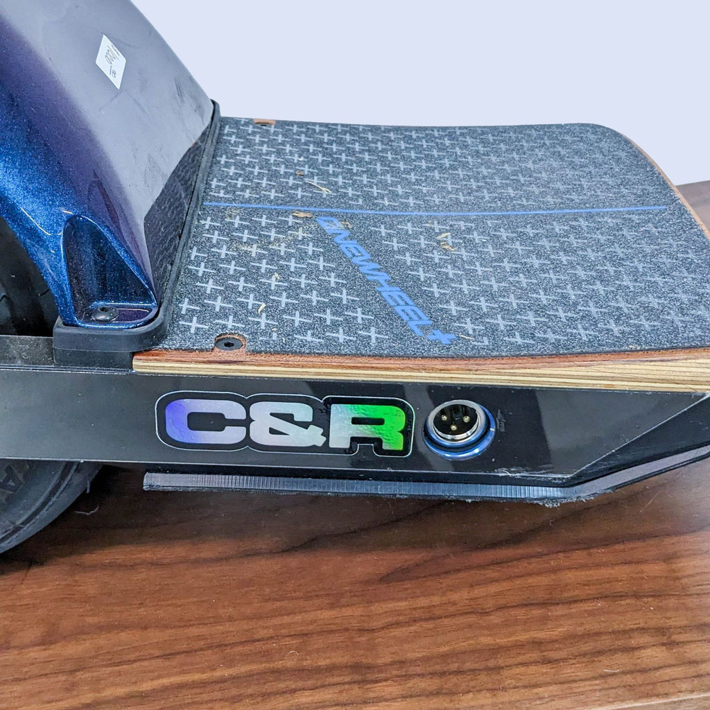 Close-up of the Onewheel's footpad and charging port, marked with "C&R".