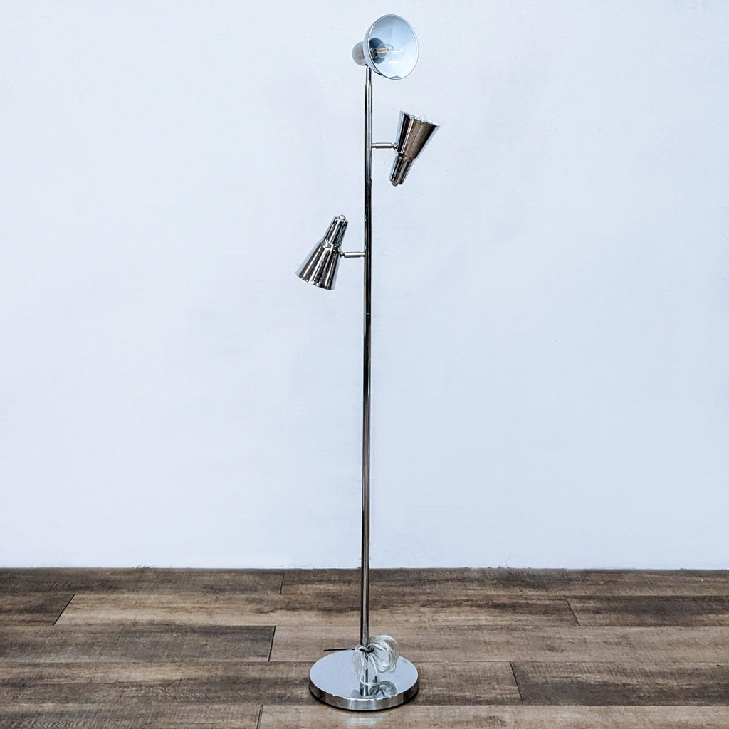 Sleek floor lamp with three adjustable chrome spotlight heads on a wooden floor.