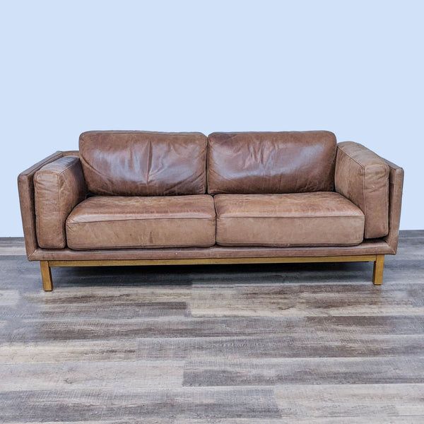 Brown leather sofa with double arms and wooden legs on a hardwood floor.