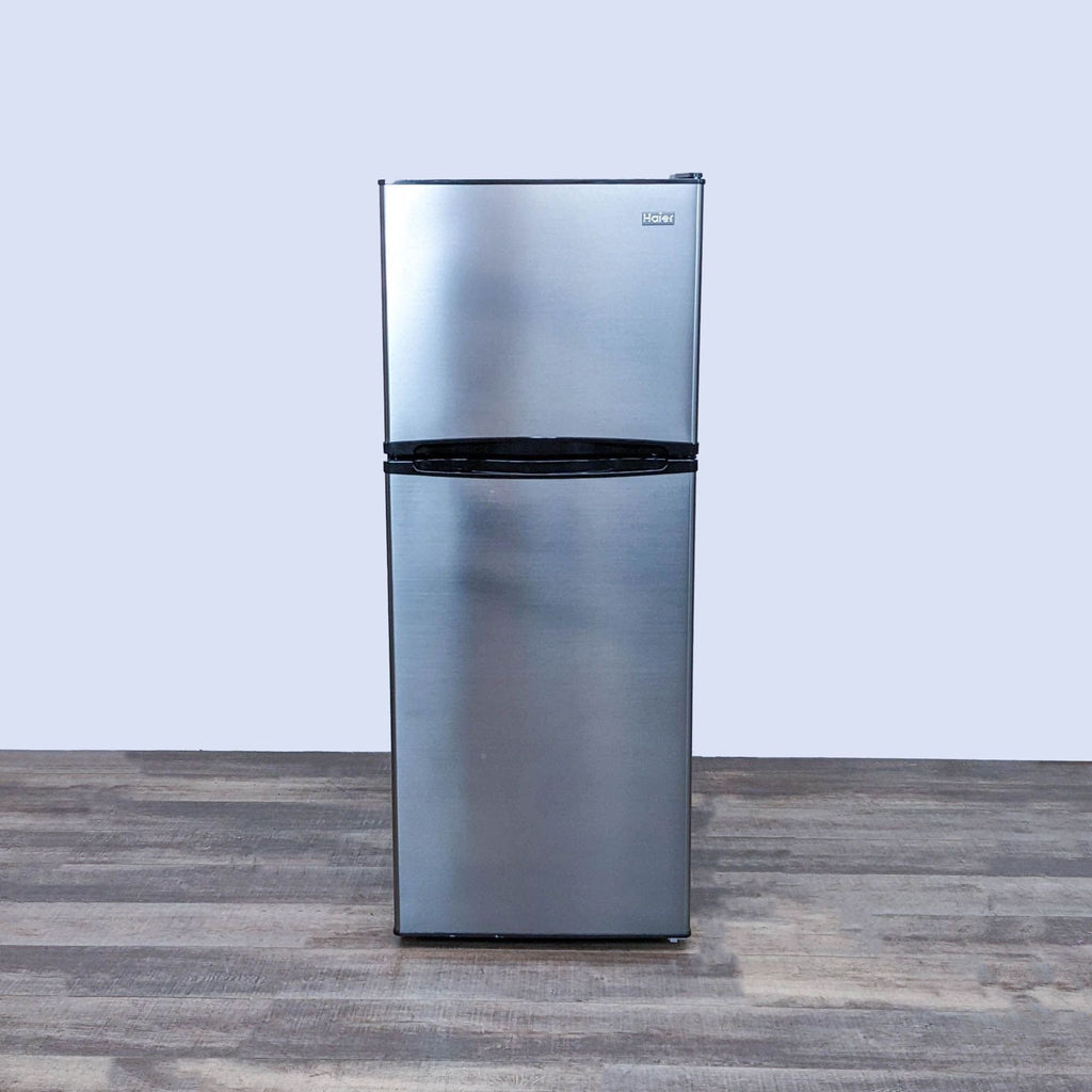Front view of a sleek Haier refrigerator on a wooden floor.