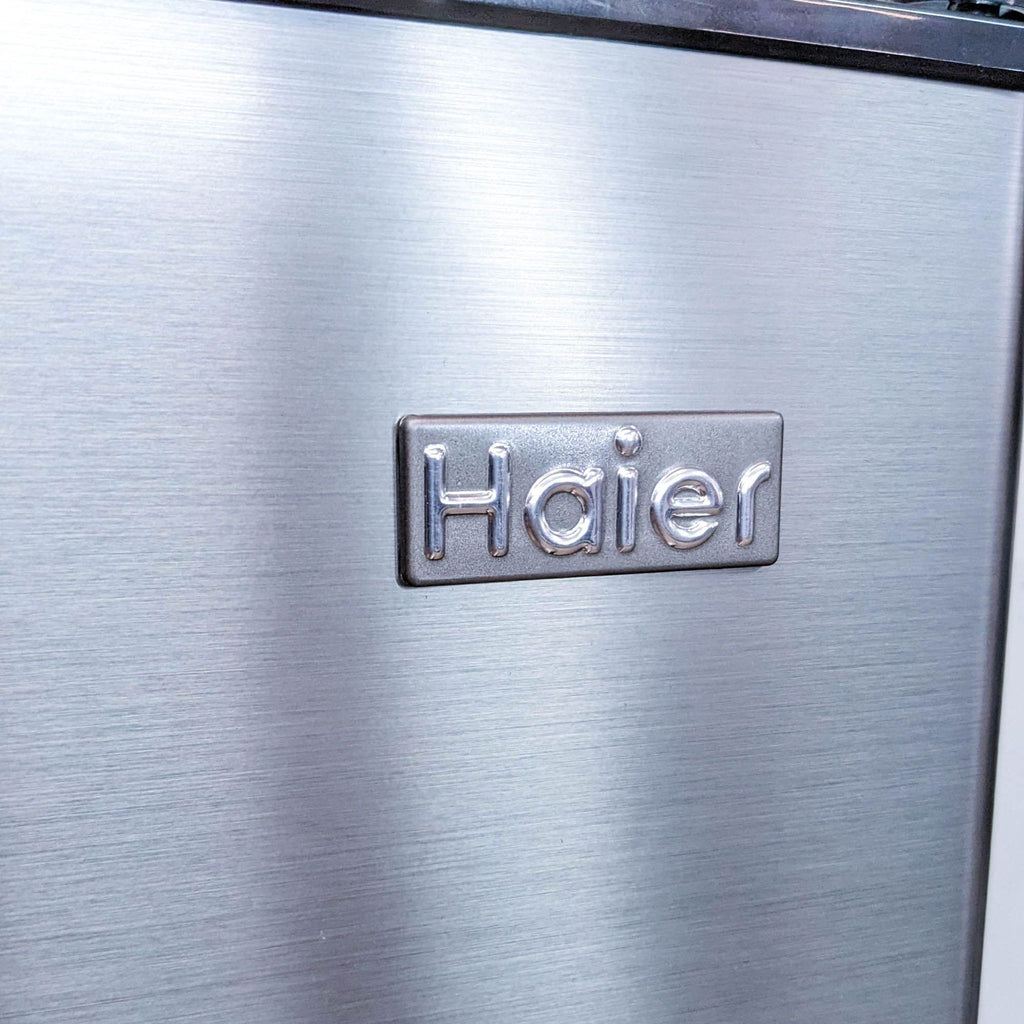 Close-up of the Haier logo on the refrigerator's stainless steel finish.