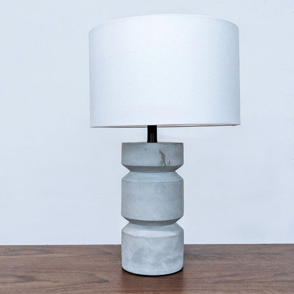 Reperch lamp with geometric gray base and white shade on a wooden surface.