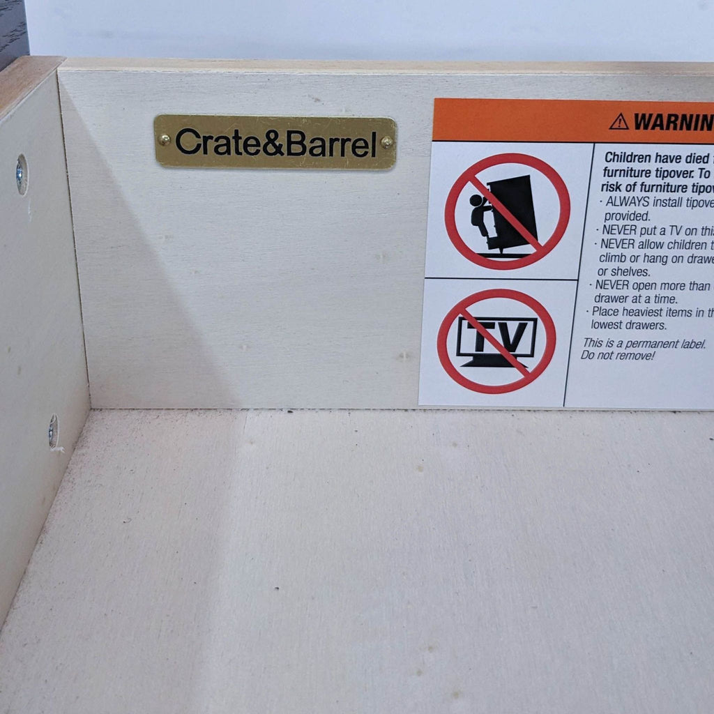 Drawer interior of Crate & Barrel chest, featuring brand plaque and safety warnings.