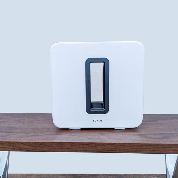 Front view of a white Sonos subwoofer on a wooden table.  