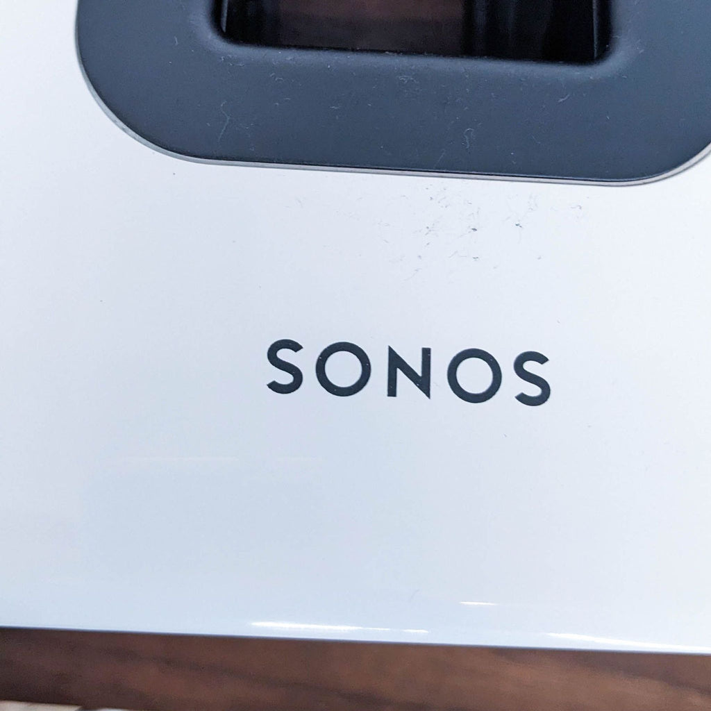 Close-up of the Sonos logo on a white subwoofer.