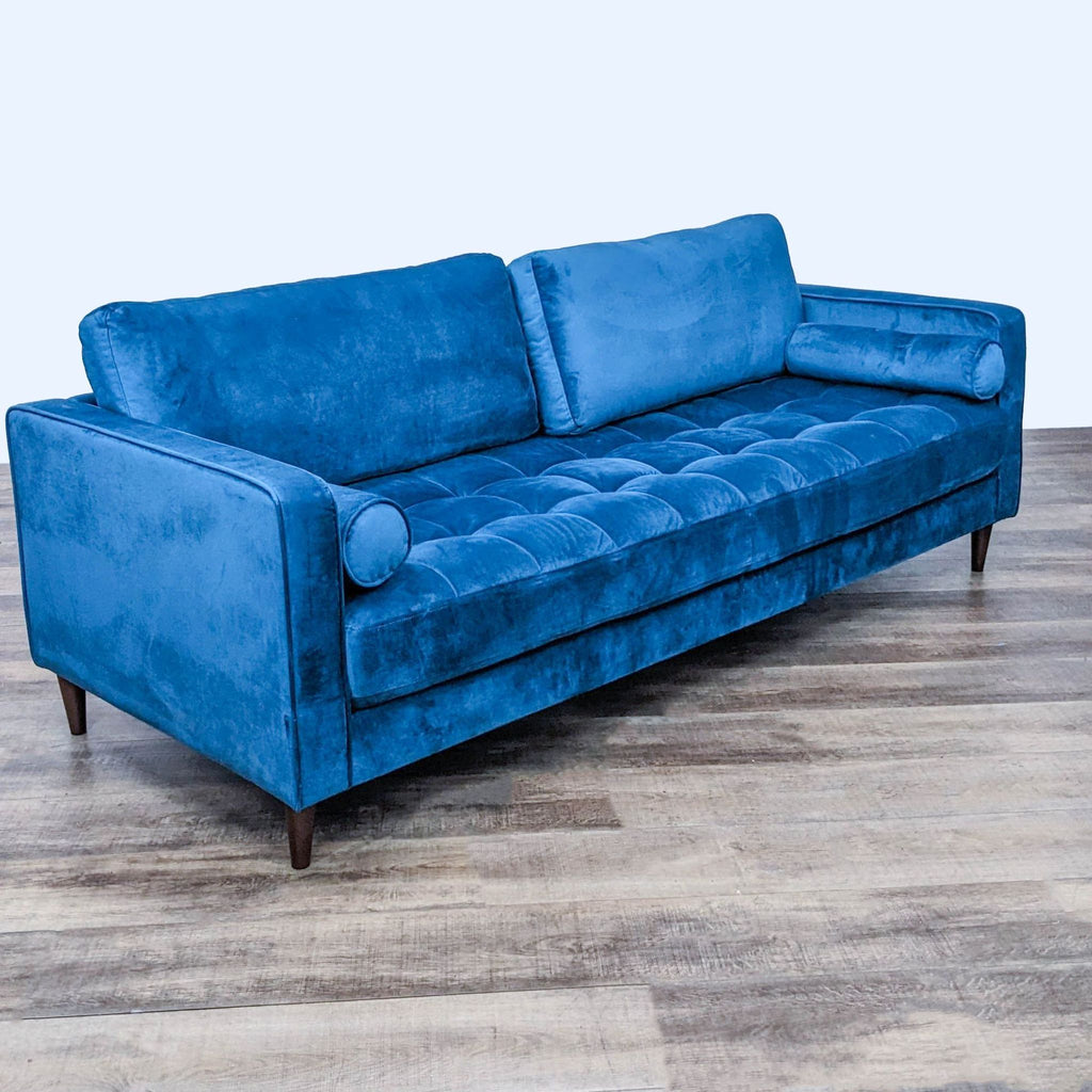 Blue velvet sofa with tufted seat, narrow arms, and bolster pillows. Features tapered legs.