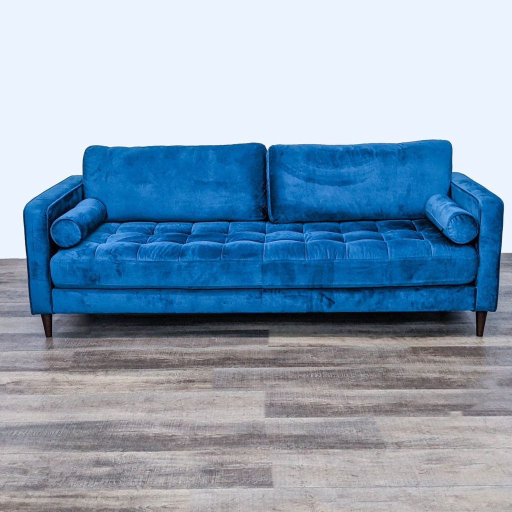 Front view of blue velvet tufted 3-seat sofa with bolster pillows and narrow arms.