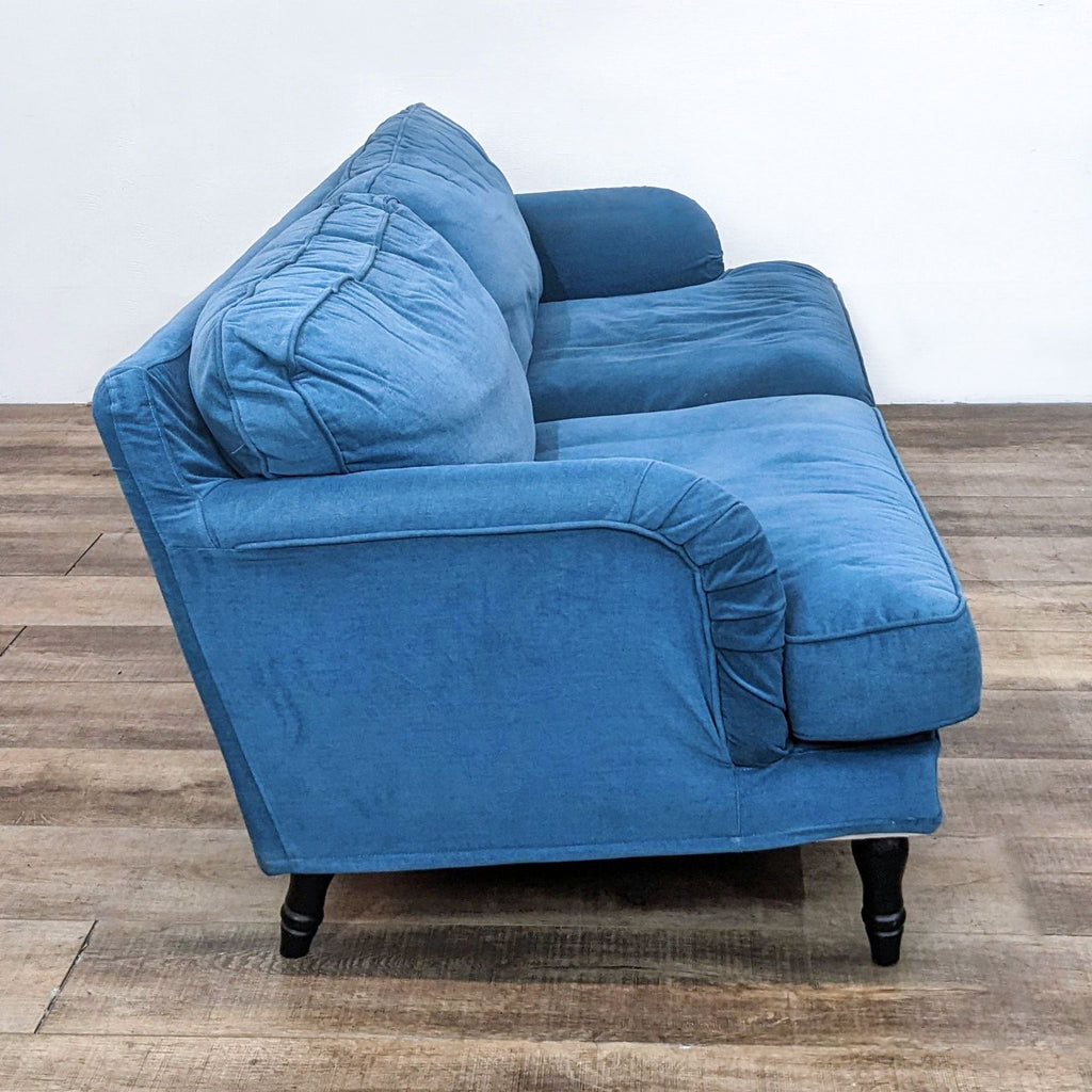 Side view of a compact blue sofa on a wooden floor.